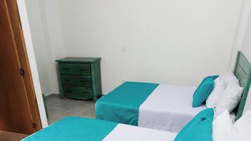Dos camas individuales con ropa de cama verde azulada y blanca, una mesita de noche de madera y una pared blanca.