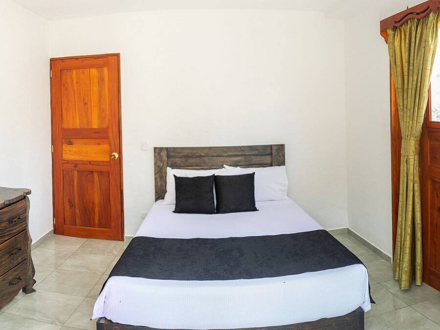 Un dormitorio con un aparador de madera, una cama con ropa de cama blanca y una ventana con cortinas.