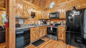 Eine holzgetäfelte Landhausküche mit einem schwarzen Kühlschrank, Edelstahlgeräten und Holzschränken.