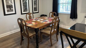Ein Esszimmer mit einem Holztisch, sechs Stühlen und einer schwarzen Arbeitsplatte. Drei gerahmte Bilder hängen an der Wand.