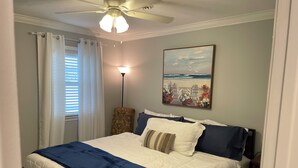 Ein Schlafzimmer mit einem Bett, einem Deckenventilator, einem Nachttisch, einer Lampe und einem Bild an der Wand.