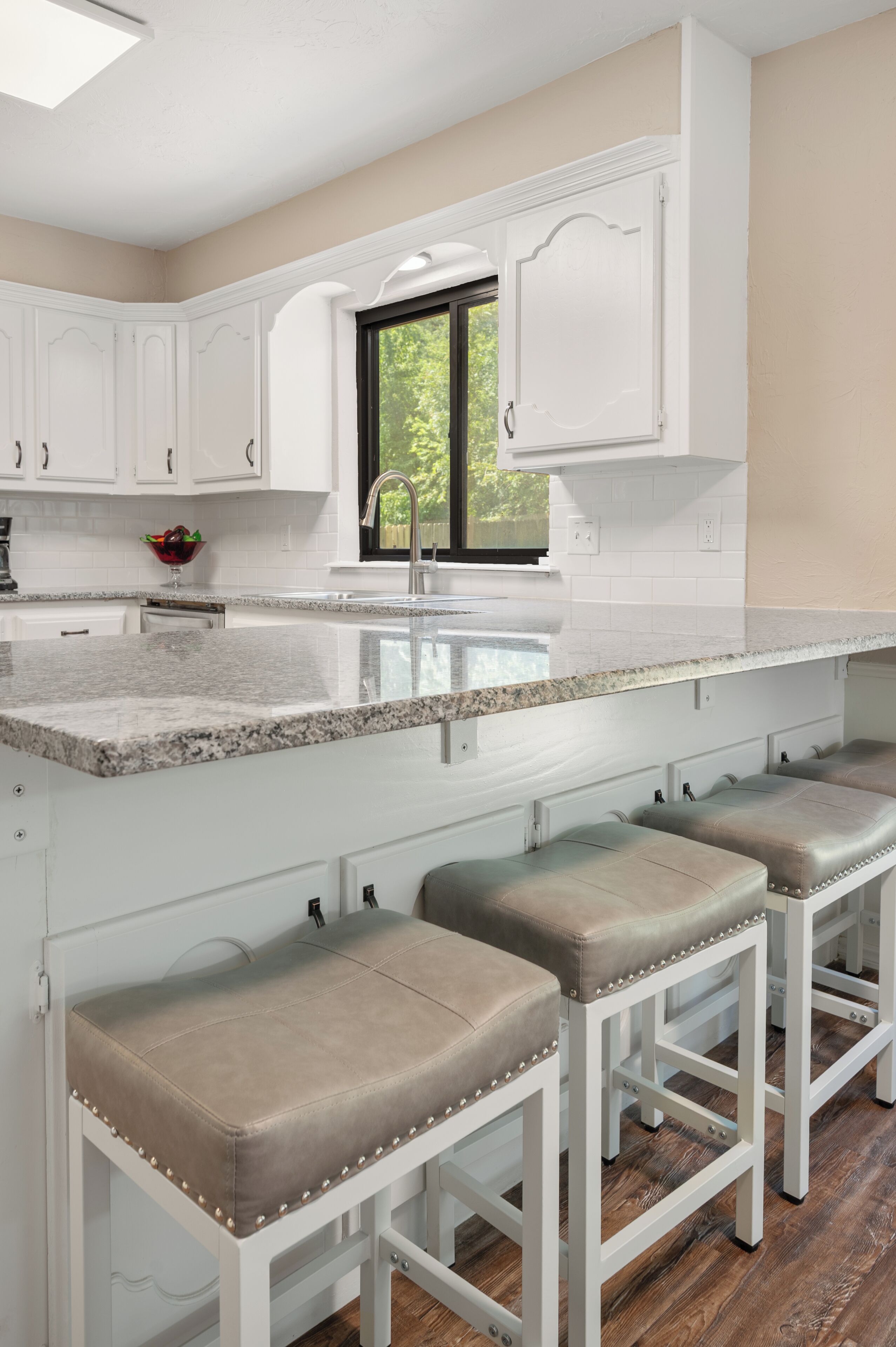 A kitchen with white cabinets, a granite countertop, and three bar stools.