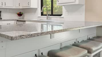 A kitchen with white cabinets, a granite countertop, and three bar stools.