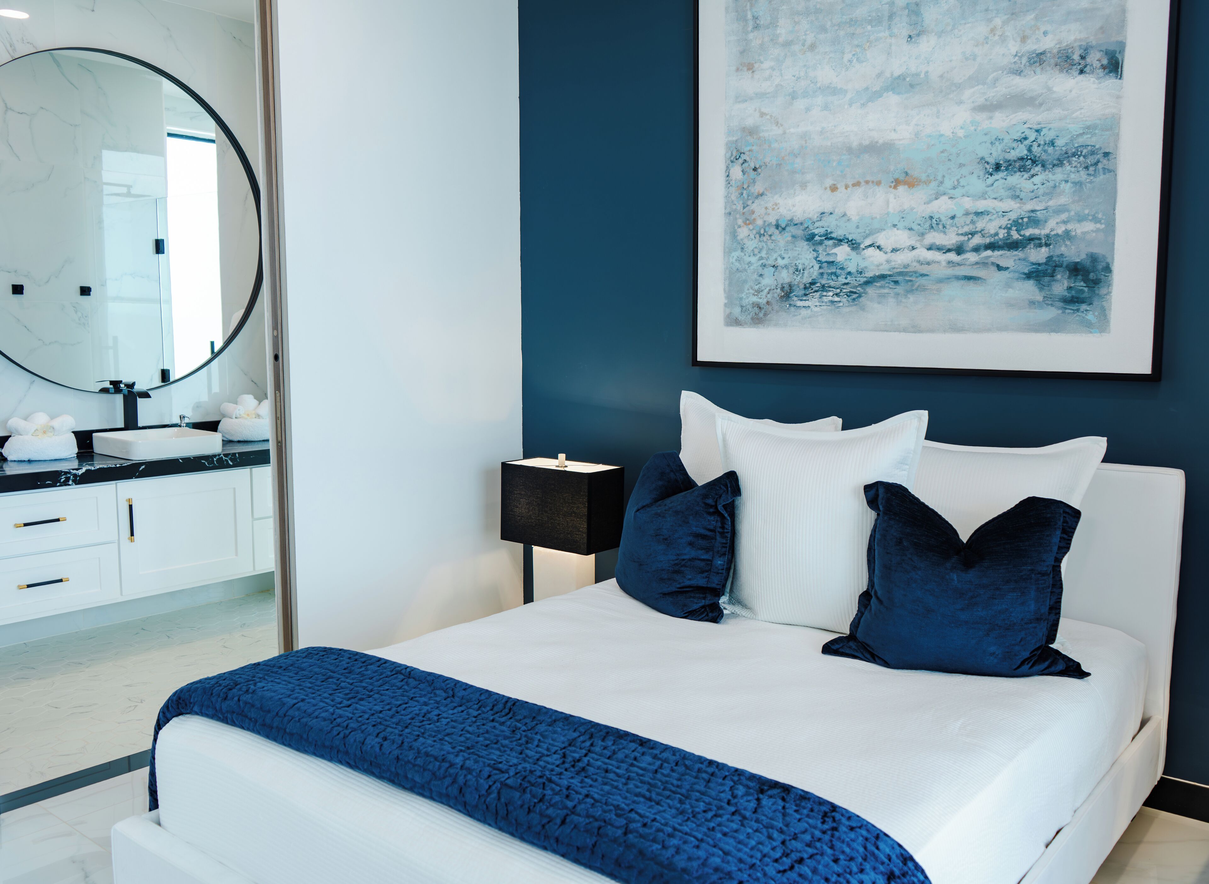A modern bedroom with a white bed, dark blue pillows, and a blue blanket.