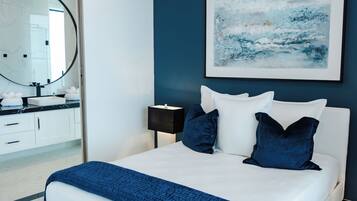 A modern bedroom with a white bed, dark blue pillows, and a blue blanket.