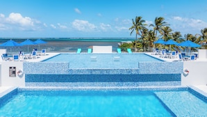 A infinity pool with a view of the ocean, surrounded by palm trees and blue umbrellas. - Clearwater Belize (San Pedro)