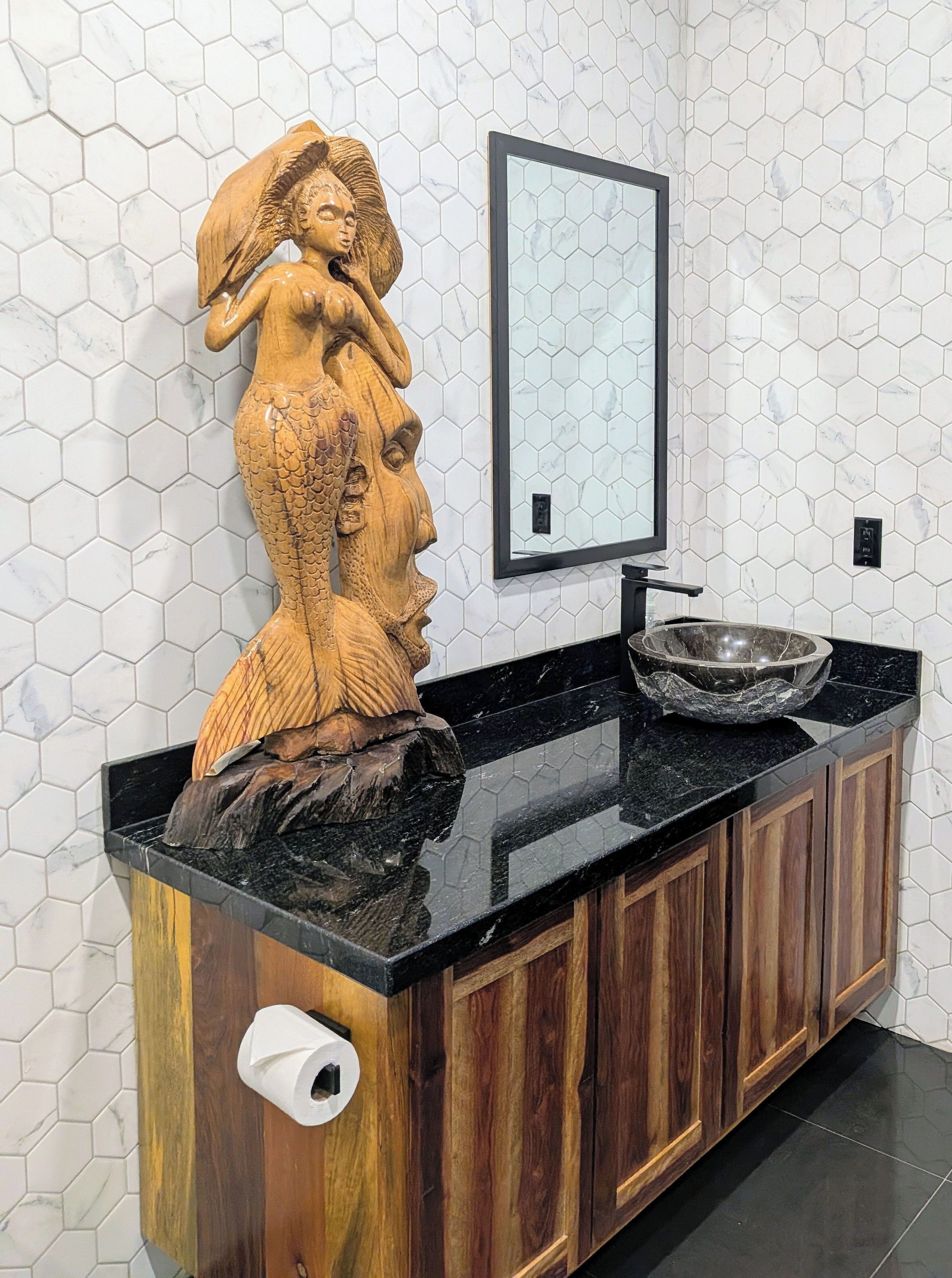 Et badeværelse med en trækommode, en marmorvask og en backsplash med hexagonfliser.