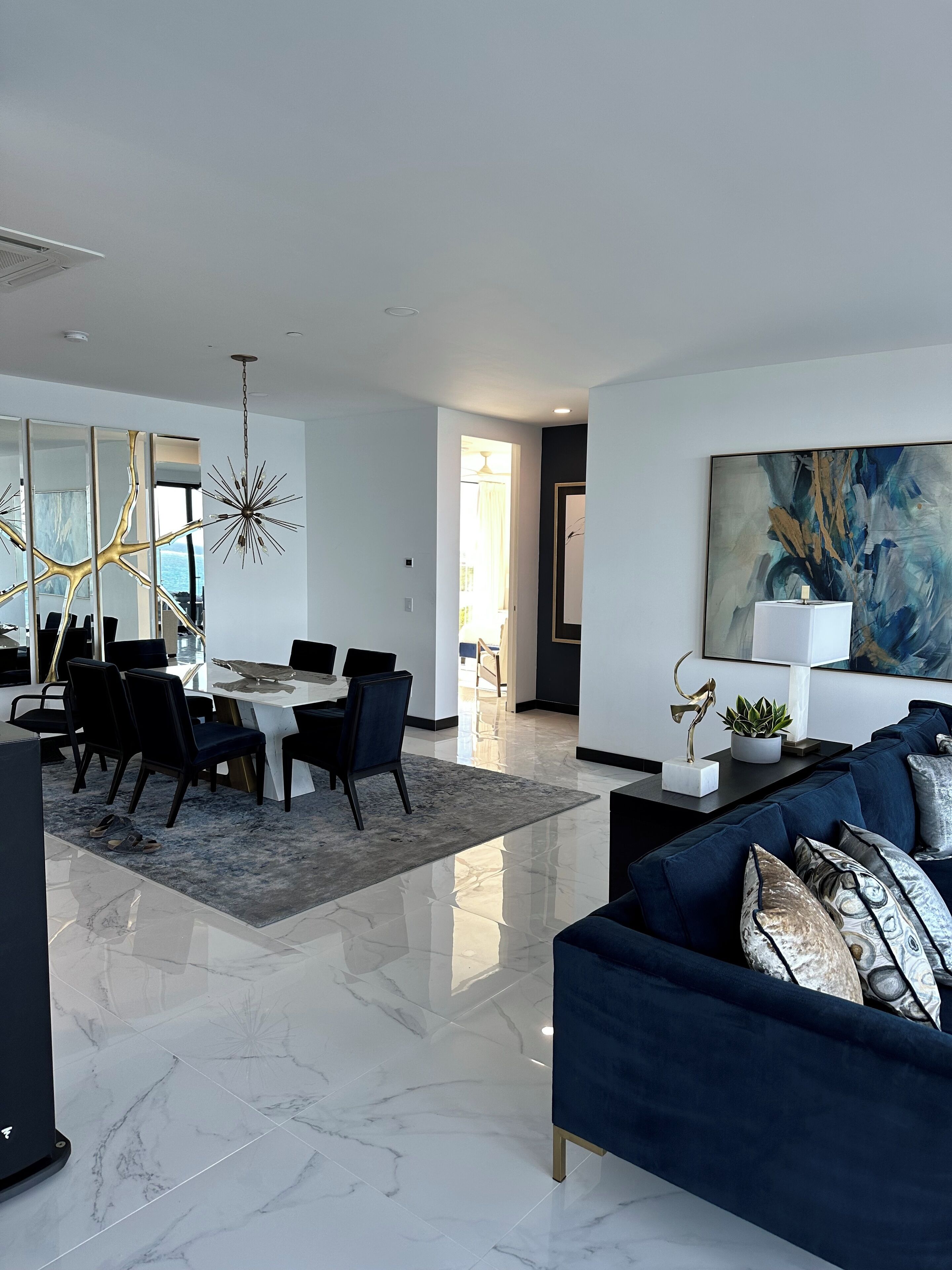 Ein modernes Wohnzimmer mit einem blauen Sofa, einem Essbereich mit weißem Tisch und Stühlen sowie einem großen abstrakten Gemälde an der Wand.