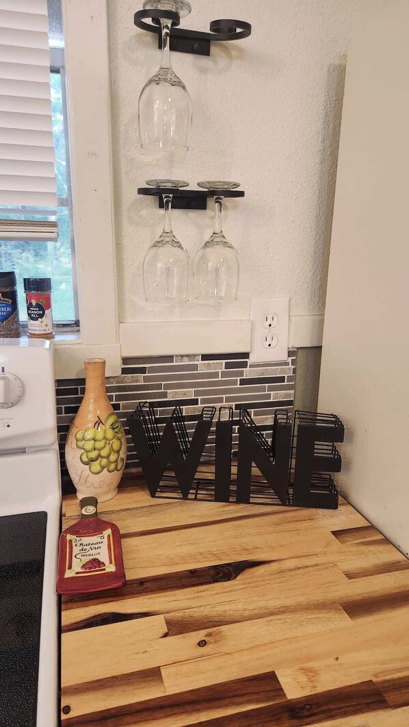 Una cocina con encimera de madera, un jarrón con uvas, una botella de Chateau de Vin Merlot y una estantería para vinos con tres copas.