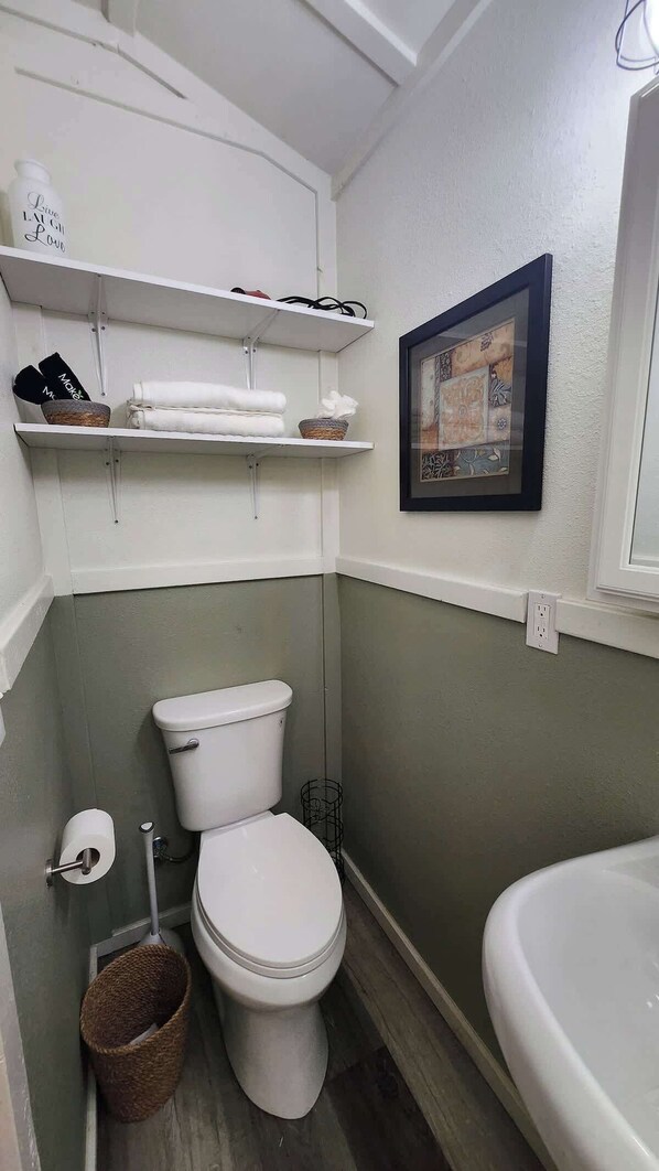 Ein kleines Badezimmer mit Toilette, Waschbecken und einem Regal über der Toilette mit Handtüchern und einer Flasche.