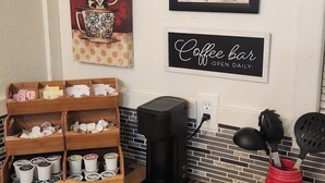 A coffee bar area with a coffee machine, a sign reading "Coffee bar - Open Daily", and a wall with a framed picture and decorative mugs. - Cozy Cabin on 22 Private Acres in Smithville, TX Peaceful Hill Country Retreat (Smithville)