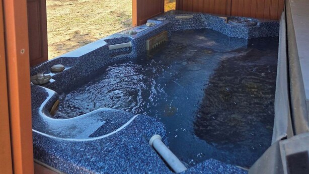 A hot tub with a wooden deck, a metal roof, and a view of a natural landscape. - Cozy Cabin on 22 Private Acres in Smithville, TX Peaceful Hill Country Retreat (Smithville)