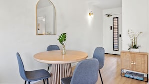 A dining area with a round wooden table, four blue chairs, a mirror, and a cabinet with a plant.