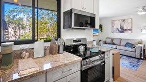 A modern kitchen with a large window, stainless steel appliances, and a cozy living area with a sofa and a painting.