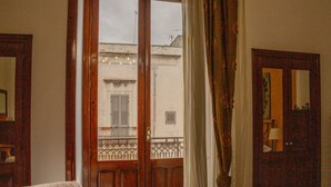 Ein Zimmer mit Holztür, einem Fenster mit Balkonblick und einem Vorhang.