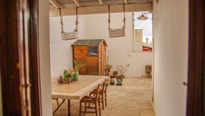 Ein rustikaler Essbereich mit Holztisch und -stühlen, umgeben von Blumentöpfen und einer kleinen Holzhütte.