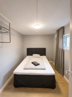A single bed with a black headboard, a bedside table, and a hanging clothes rack.