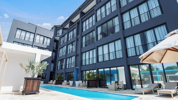 A modern building with a swimming pool, lounge chairs, and potted plants. - Modern 1BR at Rizz Suites • GYM • Pool Access • Walk to Beach • King Bed• AC ew (Sosúa)