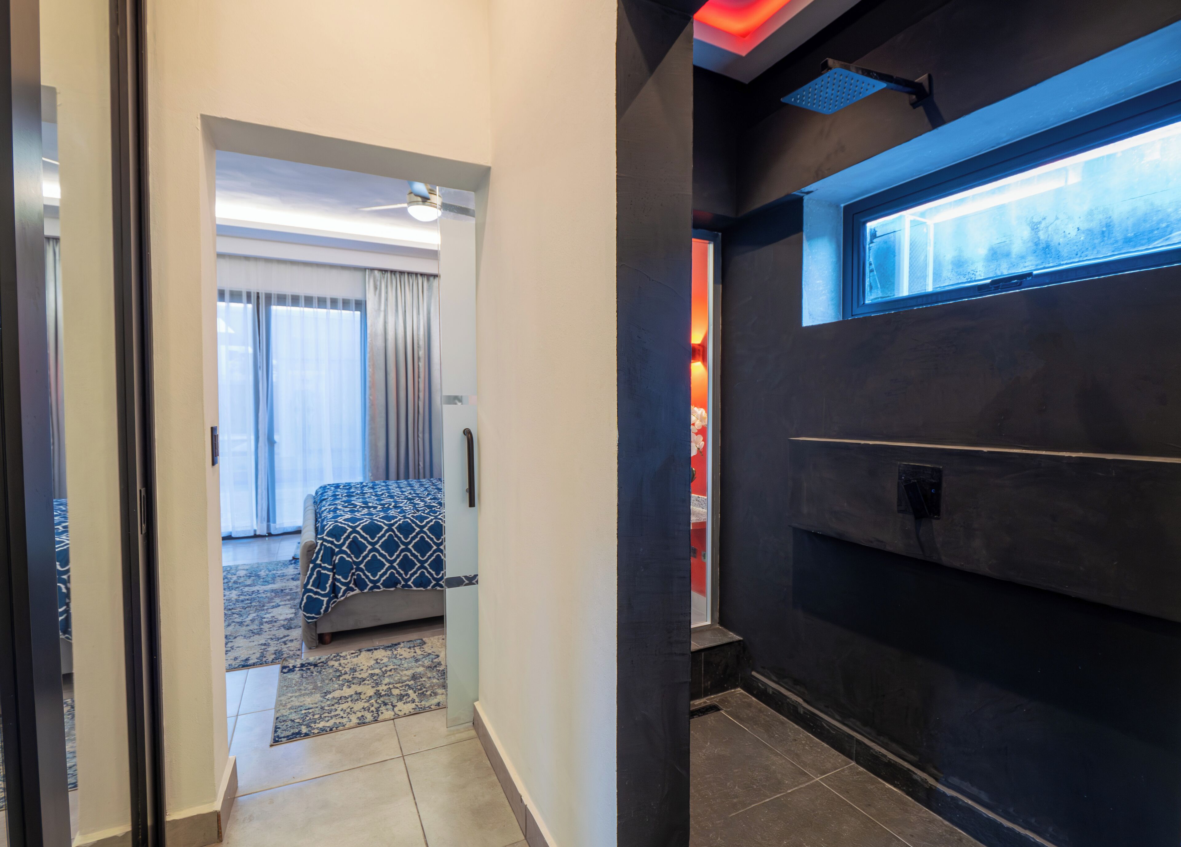 Una habitación de hotel con una cama, un ventanal, una puerta y una pared oscura.