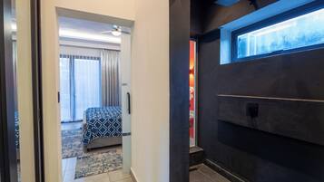 Una habitación de hotel con una cama, un ventanal, una puerta y una pared oscura.