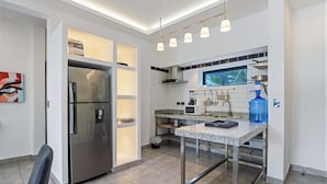A modern kitchen with a stainless steel refrigerator, a microwave, and a sink. There is a window above the sink, and a blue water dispenser on the counter. - Modern 1BR at Rizz Suites • GYM • Pool Access • Walk to Beach • King Bed• AC ew (Sosúa)