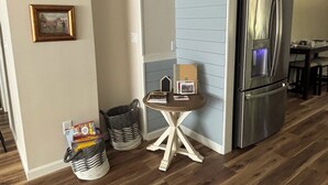 A modern kitchen with wooden flooring, a stainless steel refrigerator, and a small table with books and a picture frame.