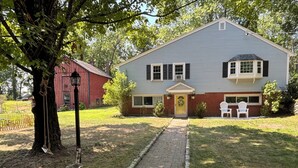 A two-story house with a front porch, a brick pathway leading to the entrance, and a red barn in the background.