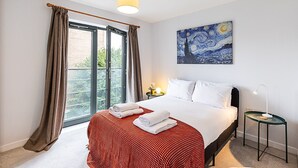 A hotel room with a bed, a painting, a nightstand, and a window with curtains.
