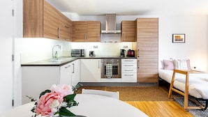 A compact kitchen with wooden cabinets, a built-in oven, and a dining area with a white table and chairs.