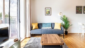 A modern living room with a grey sofa, a wooden coffee table, and a large window with curtains.