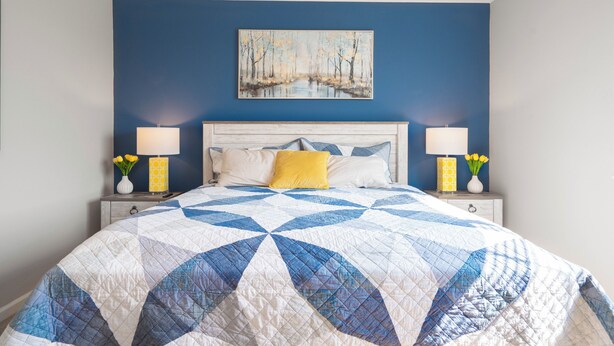 Un dormitorio con una cama grande, una pared azul y un cuadro sobre la cama.