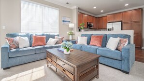 Sala de estar con un sofá azul, una mesa de centro y una cocina con armarios de madera y electrodomésticos.