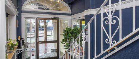 A hotel lobby with a staircase, a reception desk, and a large arched window.