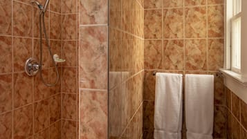 Une salle de bain avec une douche, des murs carrelés et deux serviettes blanches suspendues à un porte-serviettes.