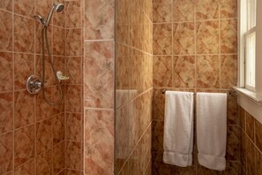 Ein Badezimmer mit Dusche, geflieste Wände und zwei weiße Handtücher an einem Haken.