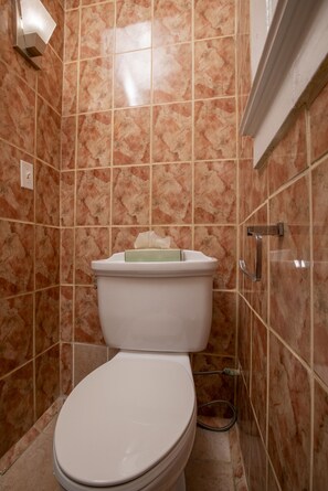Une salle de bain avec des toilettes blanches, des carreaux de marbre et une tuyauterie apparente.