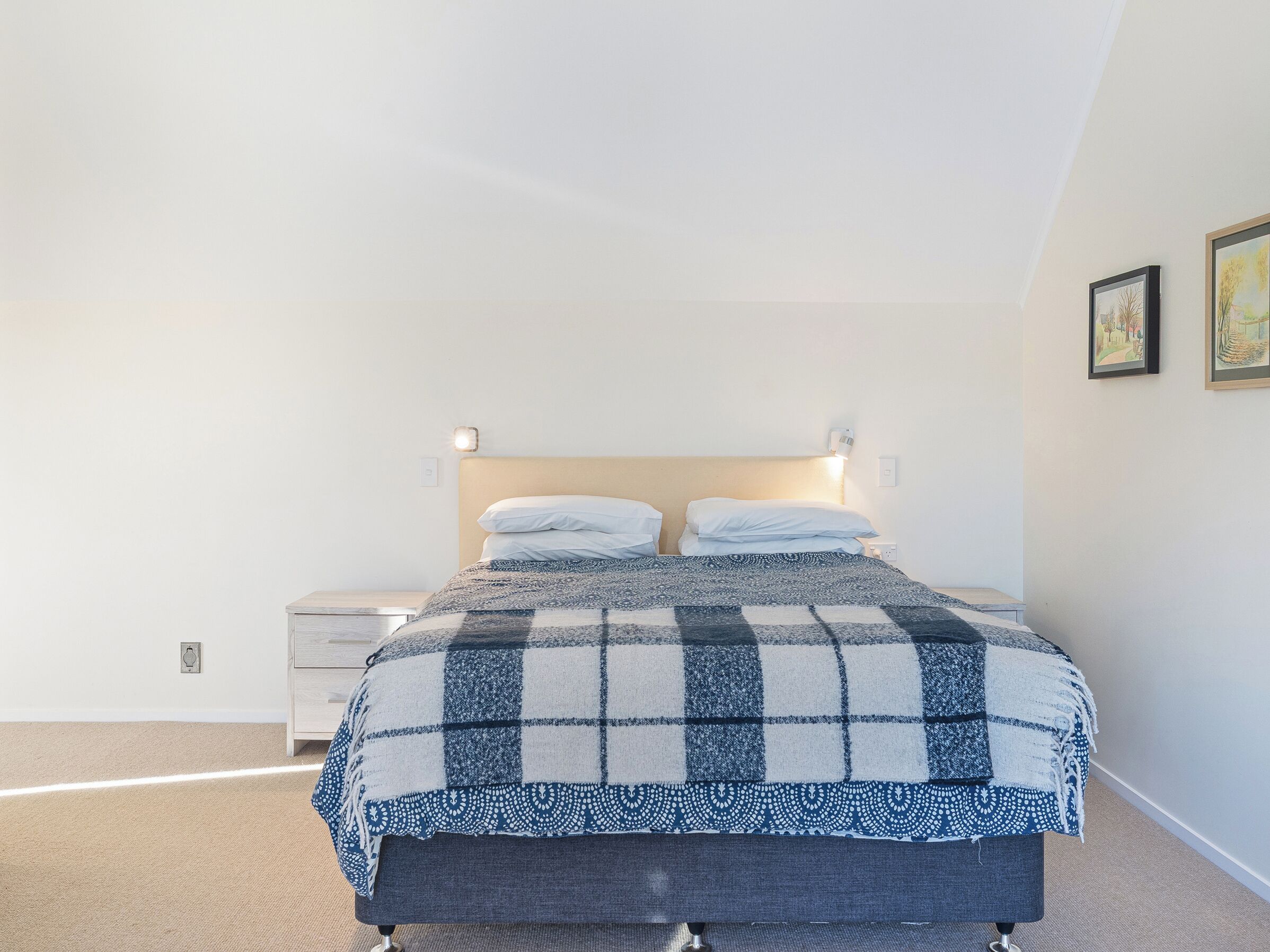 A bedroom with a bed, bedside tables, and wall-mounted lights.