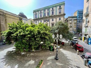 A courtyard with a large tree, a fountain, and a building with a dome in the background. - Incanto Napoli (Naples)