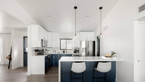 A modern kitchen with white cabinets, a central island with bar stools, stainless steel appliances, and pendant lighting. - Chic Scottsdale Stay | Pool, Hot Tub! (Scottsdale)