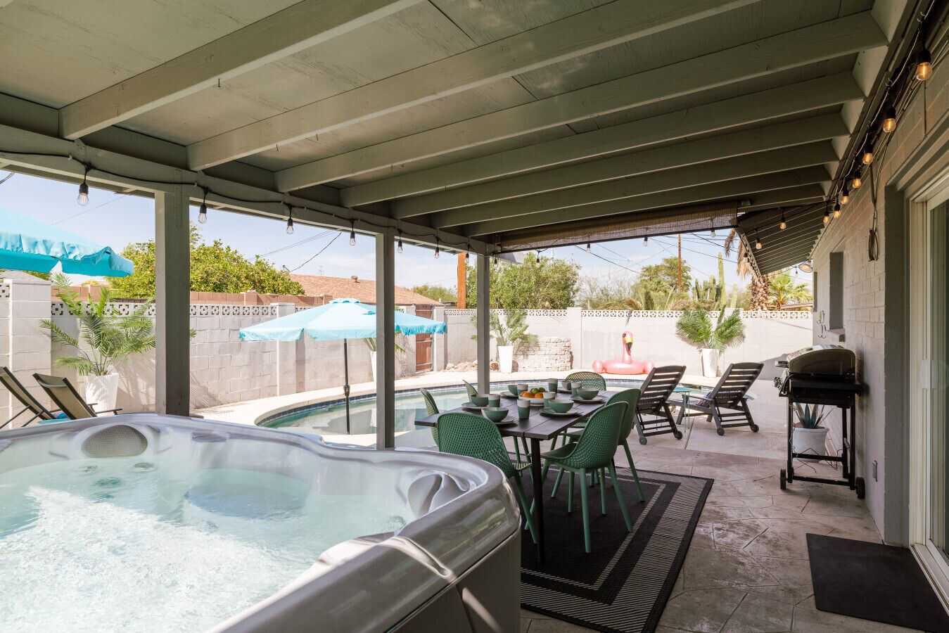 A covered patio with a hot tub, outdoor seating, and a barbecue grill.