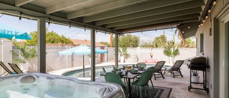 A covered patio with a hot tub, outdoor seating, and a barbecue grill.