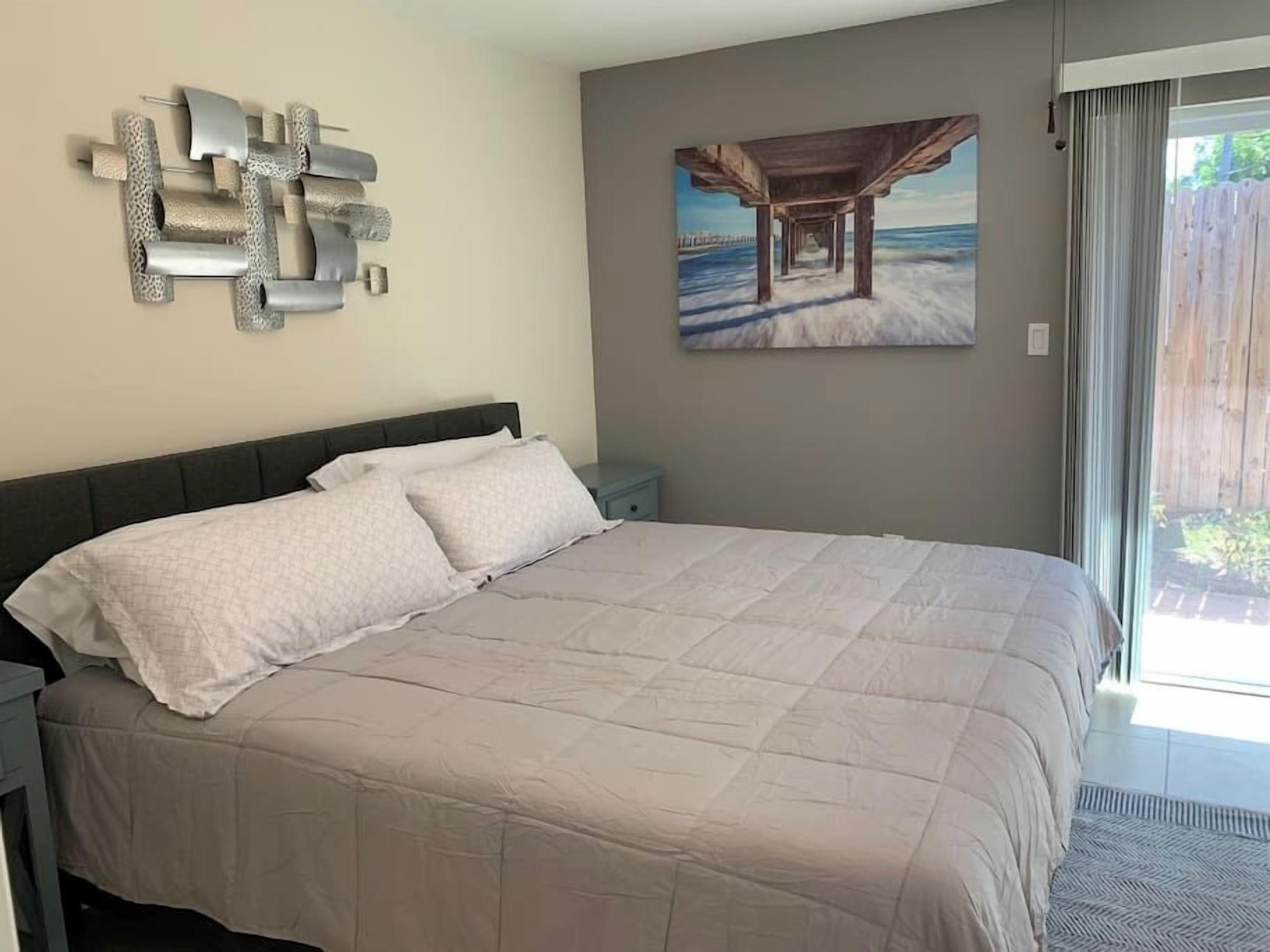 Ein Schlafzimmer mit einem großen Bett, einem Nachttisch, einem an der Wand befestigten abstrakten Kunstwerk und einem Gemälde eines Piers.
