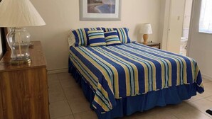 Un dormitorio con una cama, un aparador de madera, un cuadro enmarcado en la pared y una puerta que da a otra habitación.