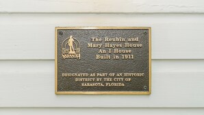 Una placa en una pared blanca indica que la Casa Reubin y Mary Hayes es una Casa I construida en 1911 y designada como parte de un distrito histórico por la ciudad de Sarasota, Florida.