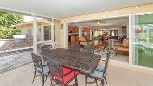 A covered patio with a dining table and chairs, a kitchen area, and a living room with a sofa and chairs.