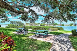 A park with picnic tables, a paved walkway, and a body of water in the background.