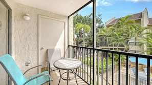 A balcony with a chair, a small table, and a view of a residential area with trees and a building. - Huge Heated Pool ❤ Short Walk to the Beach, ride FREE Trolley around the Key! (Siesta Key)