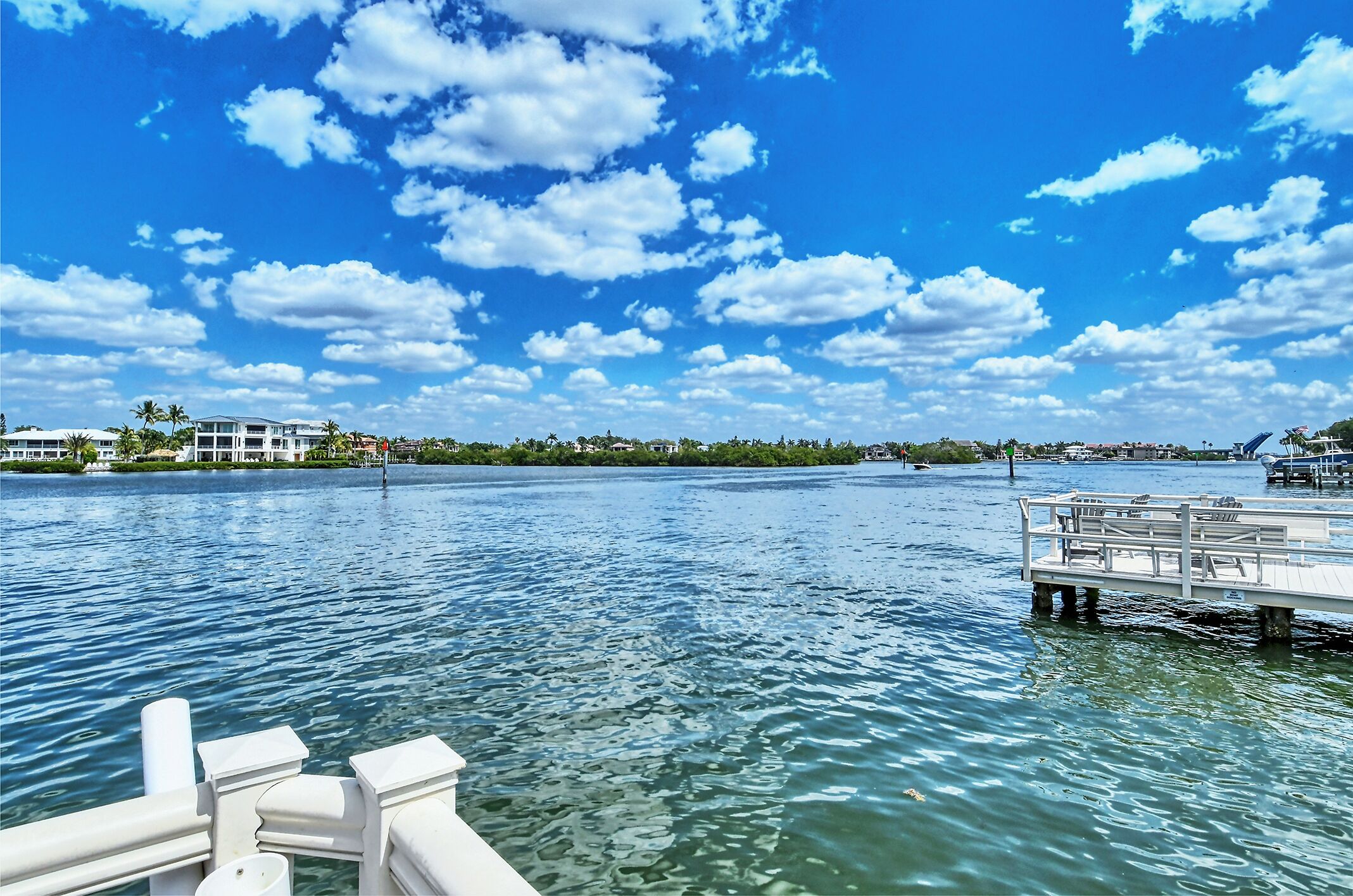 A waterfront view with a dock, calm water, and buildings in the background.