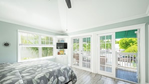 Un dormitorio con cama, televisor, ventana y balcón con vista a follaje.