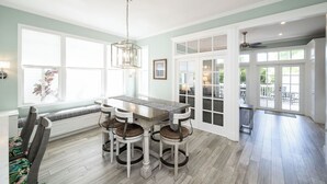 Un comedor con mesa y sillas, un banco y vistas al exterior a través de ventanas amplias.